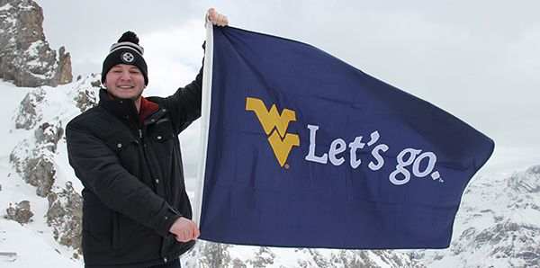 Male student on snowy mountain in Germany holding a WVU Let's Go flag